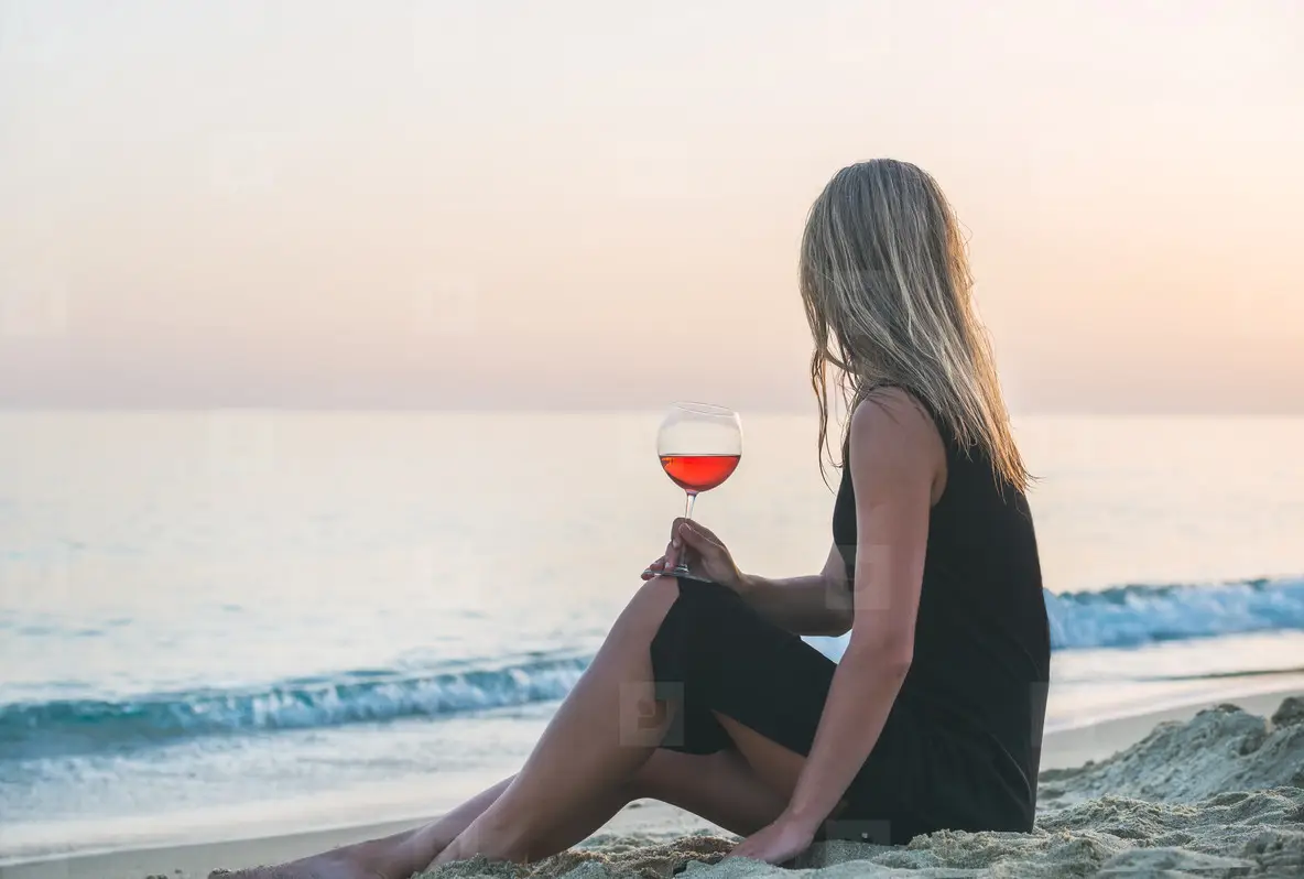 Young Blond Woman Enjoying Glass Of Rose Wine On Beach By The Sea