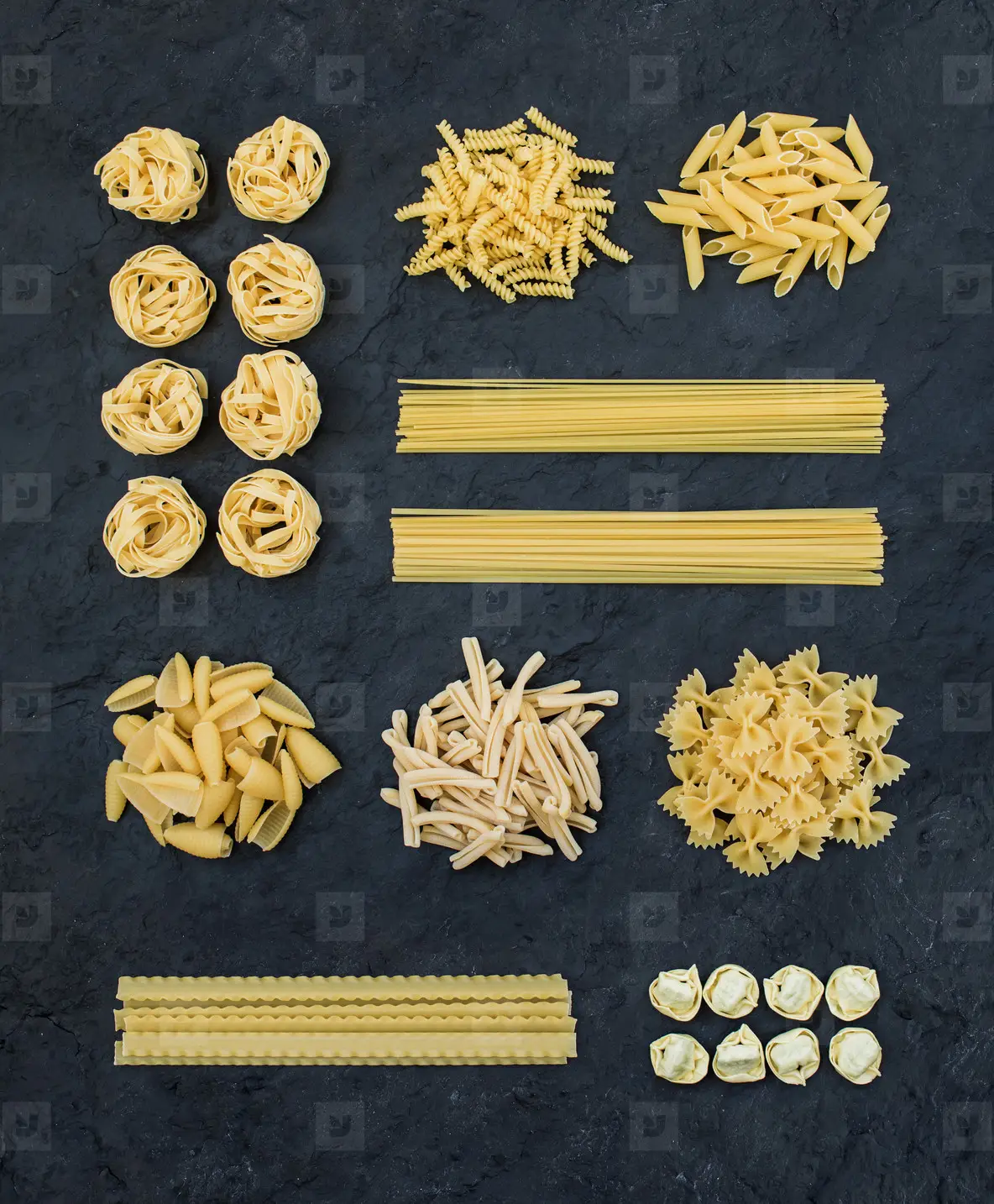 Different types of Italian uncooked pasta on black slate stone background  top view