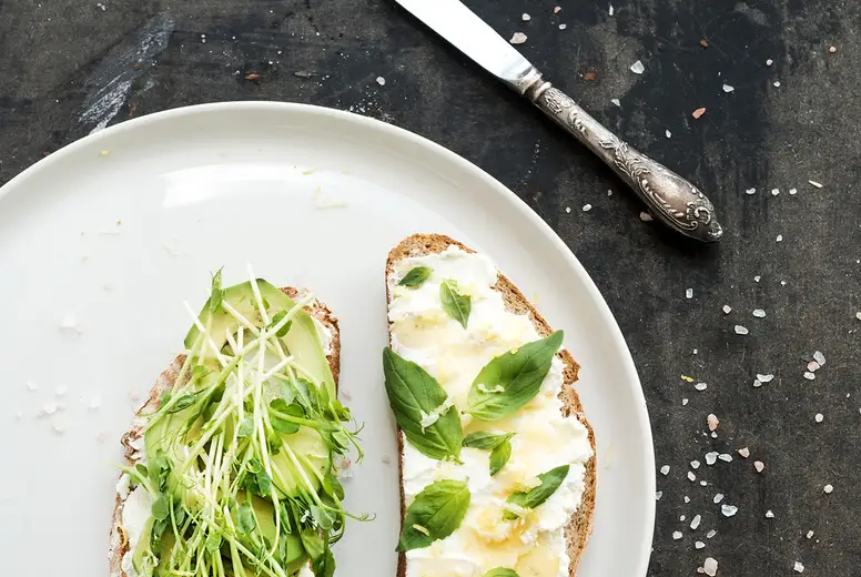 Avocado, ricotta, basil and sprout sandwiches on white ceramic plate over dark grunge backdrop, top view