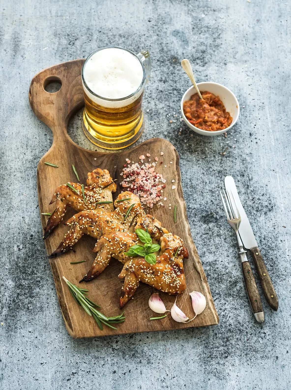 Fried chicken wings on rustic serving board  spicy tomato sauce  herbs and mug of light beer over black wooden backdrop