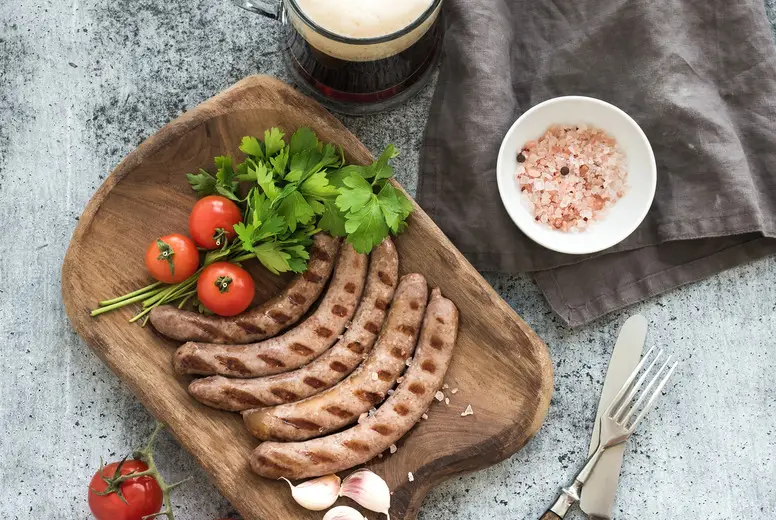 Grilled sausages with vegetables on rustic serving board and mug of light beer over grunge  backdrop.