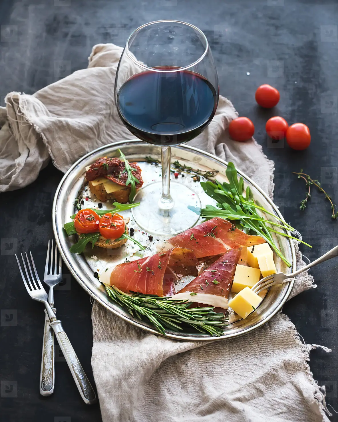 Wine appetizer set  Glass of red wine  vintage dinnerware  brushetta with cherry  dried tomatoes  arugula  parmesan  smoked meat on silver tray over rustic grunge surface