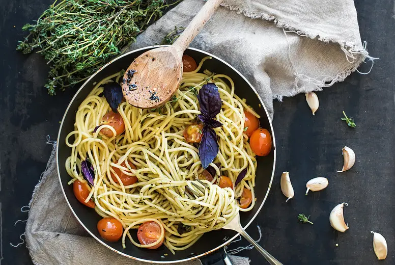 Pasta spaghetti with pesto sauce, basil, cherry-tomatoes, garlic and thyme in a cooking pan on old grunge dark table