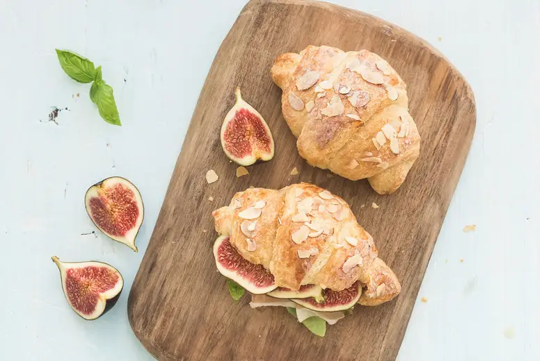 Freshly baked croissants with fresh figs and prosciutto on serving board over blue rustic wooden backdrop