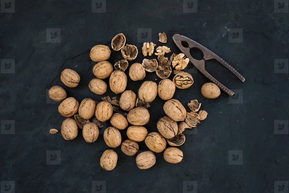 Walnuts with nutcracker over  black slate stone background