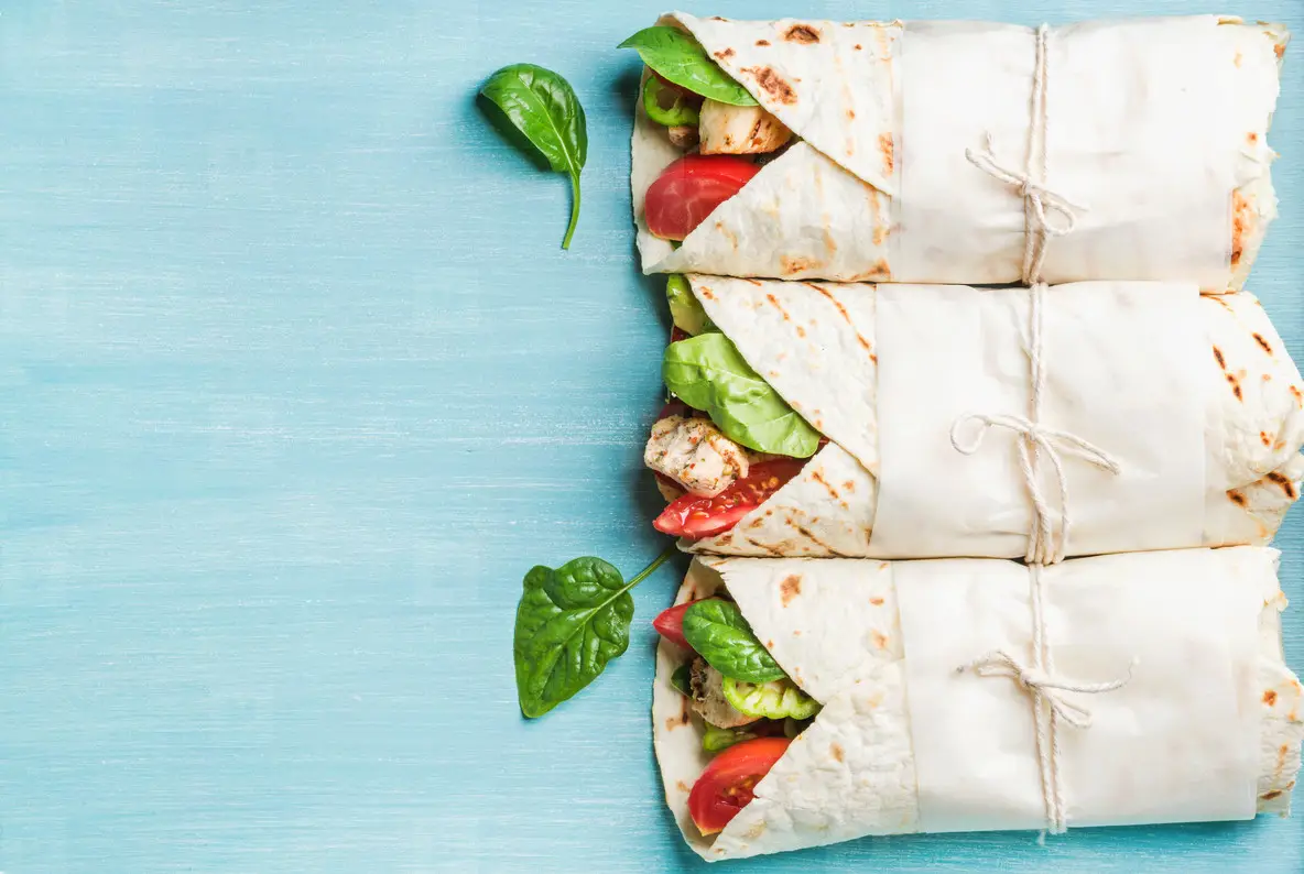 Healthy lunch snack  Three tortilla wraps with grilled chicken fillet and fresh vegetables over turquoise blue painted wooden background  Top view  copy space