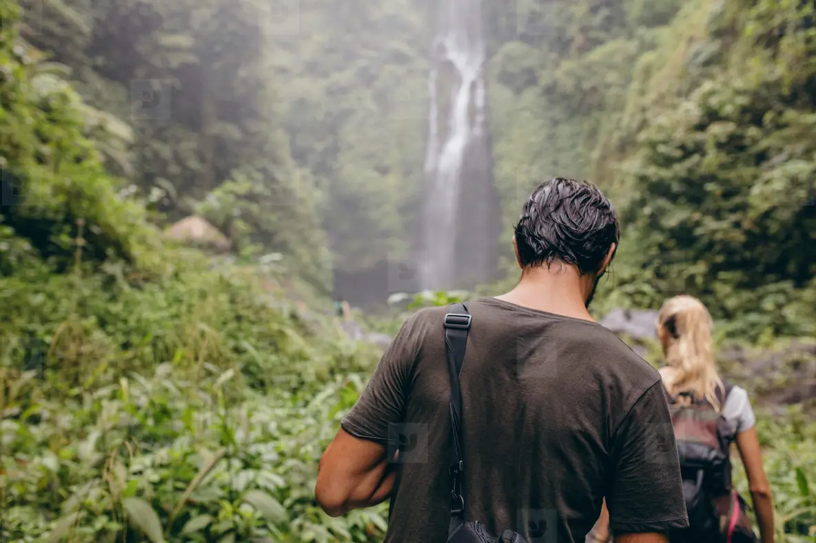 Couple of tourists walking towards a waterfall in forest