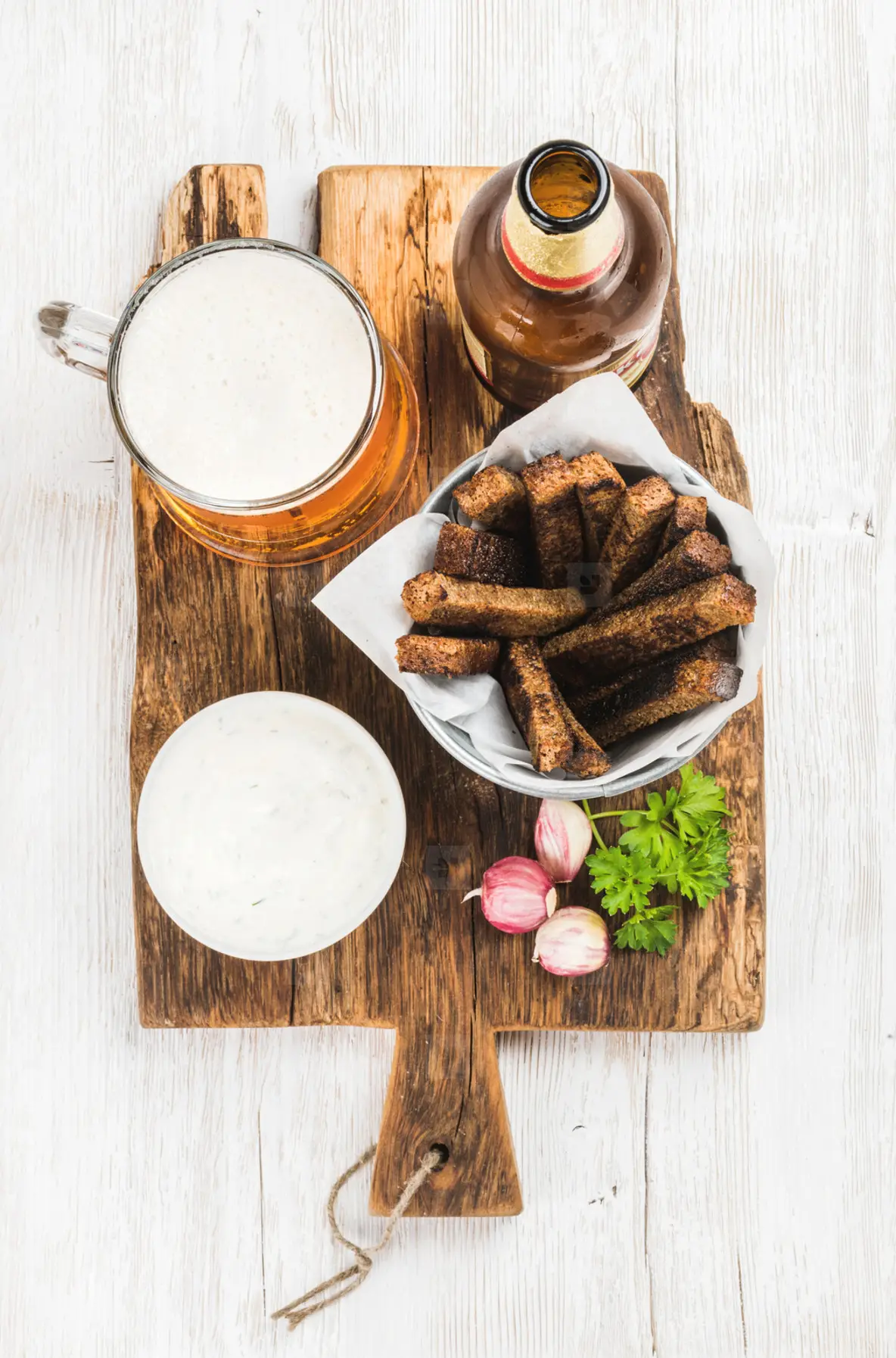 Beer snack set  Pint of pilsener in mug  open glass  bottle  rye bread croutons with garlic cream cheese sauce on rustic wooden board over white painted old  background