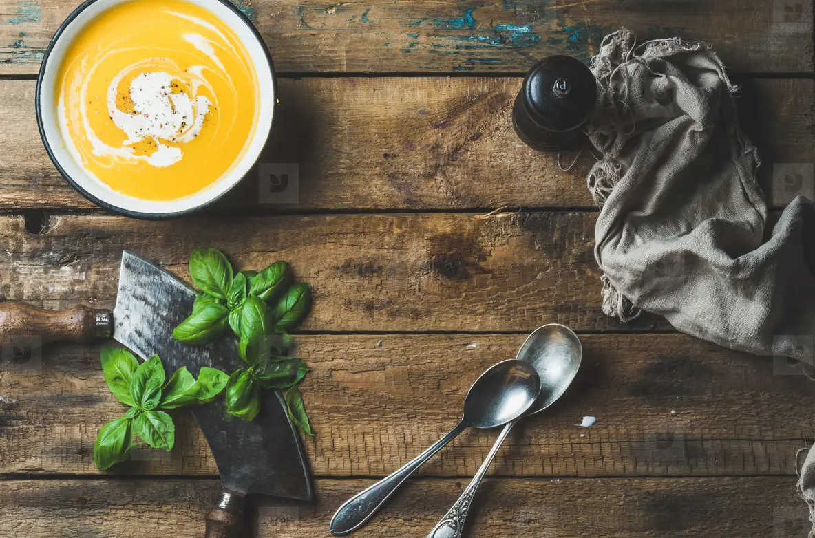 Pumpkin cream soup in bowl with fresh basil and spices