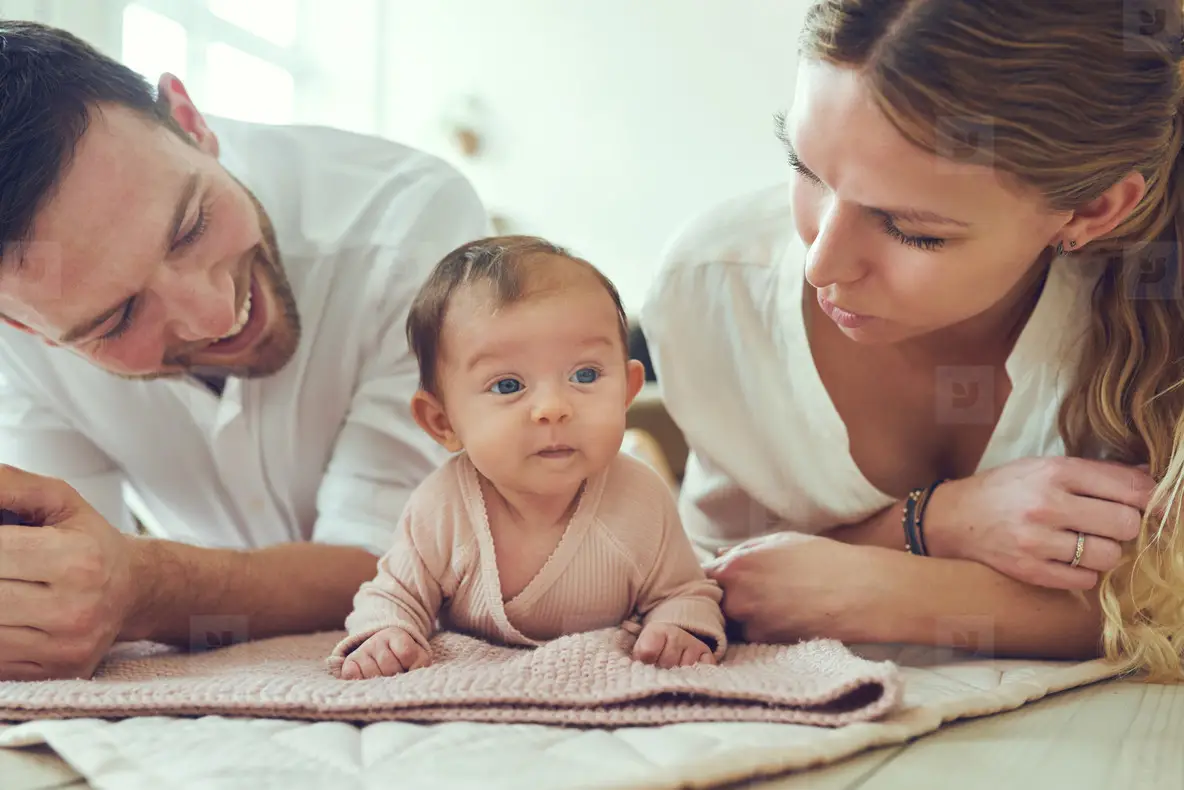 Smiling Young Parents Lying With Their Baby Girl At Home Photo