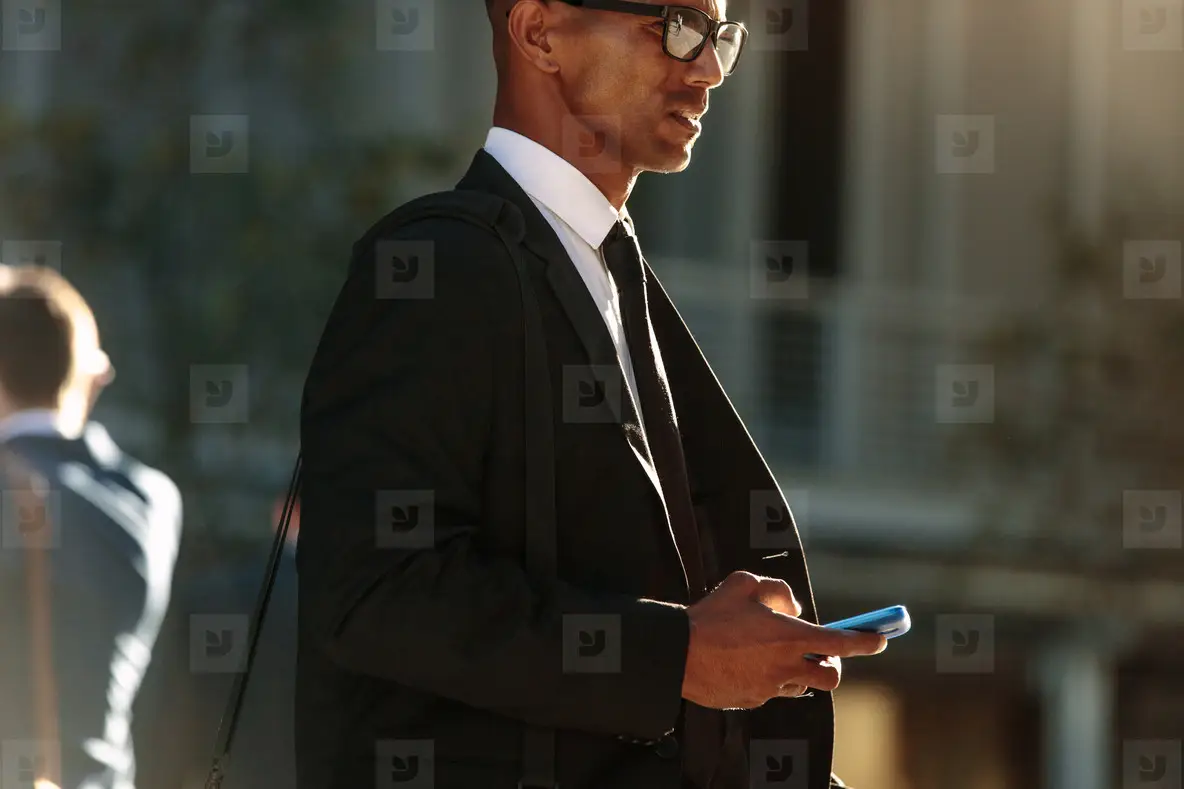 Man using mobile phone while walking on street to office