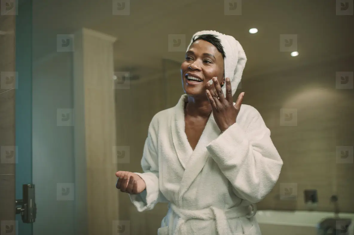 Reflection in mirror of female applying cream on face