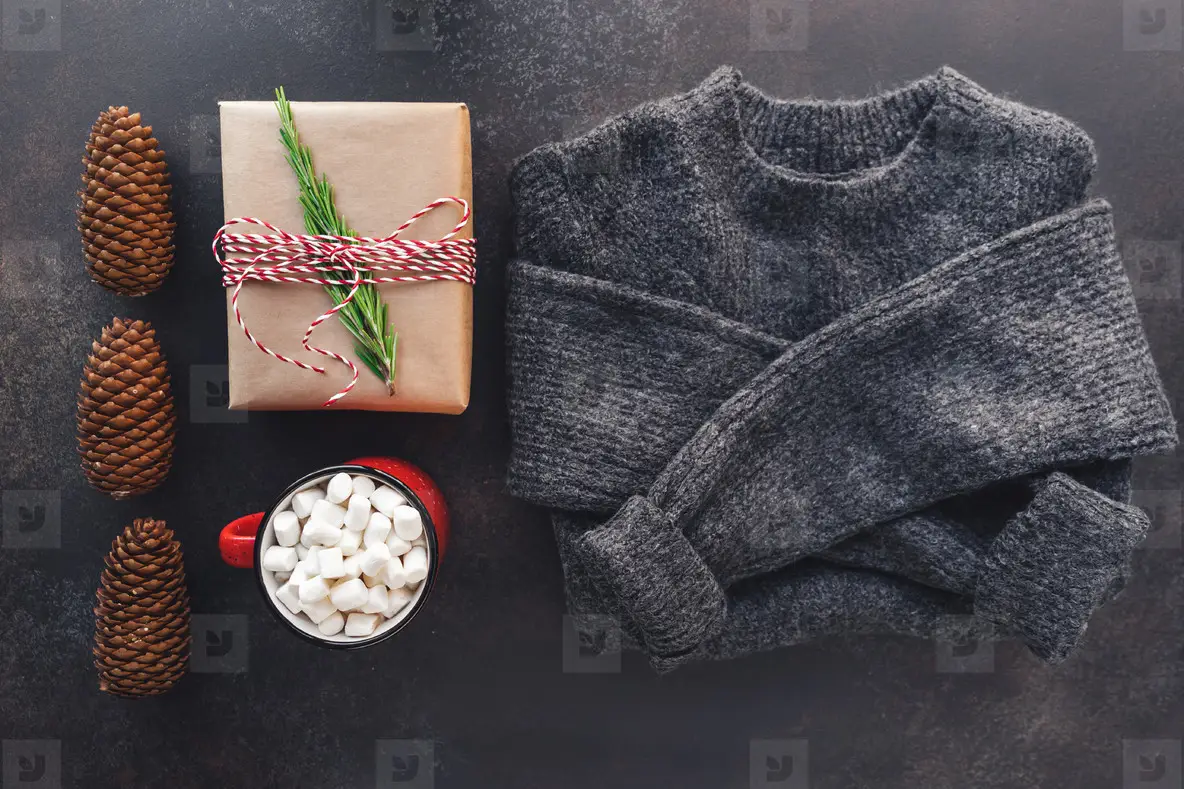 Top view of Christmas or winter time flat lay with hot chocolate  gift box and a woolen sweater on a dark background