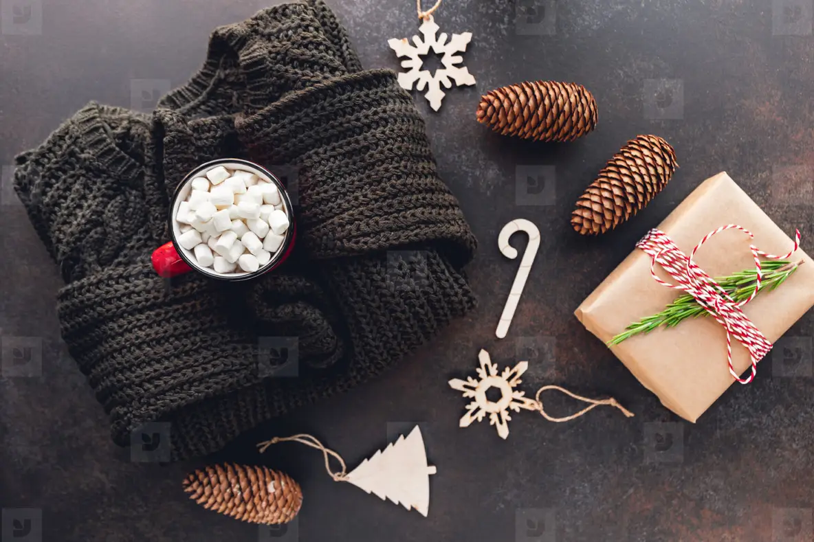 Hot chocolate in a red mug with marshmallow surrounded Christmas decoration on a woolen sweater