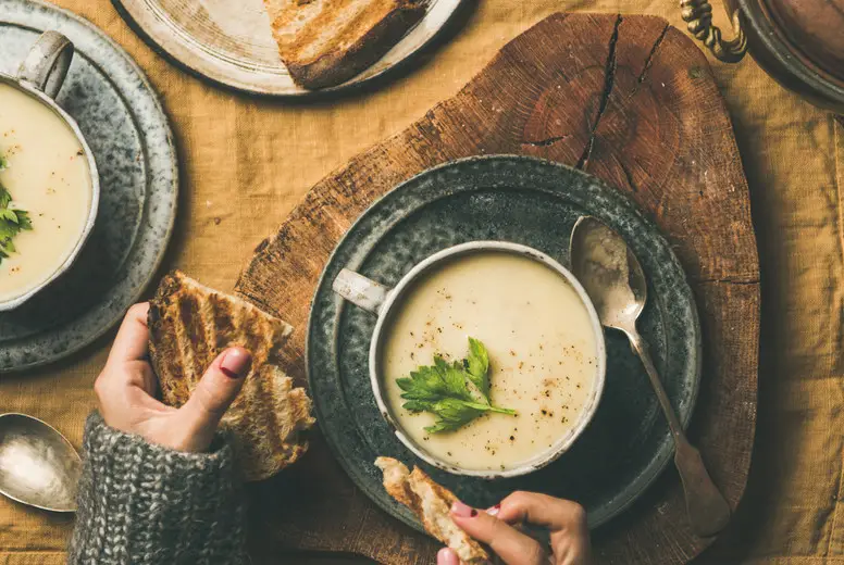 Celery cream soup and female hands with bread, square crop