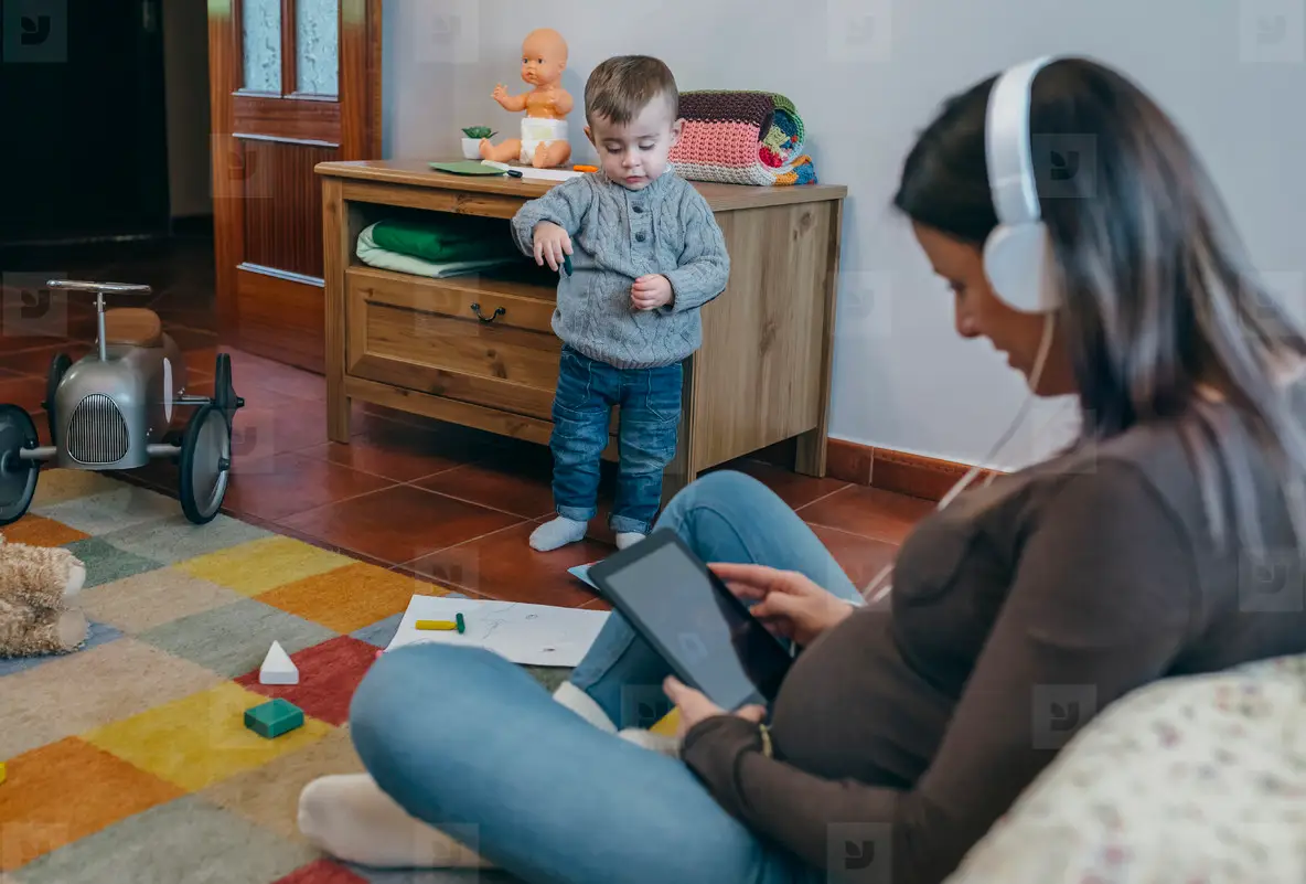 Pregnant using the tablet while her son is playing