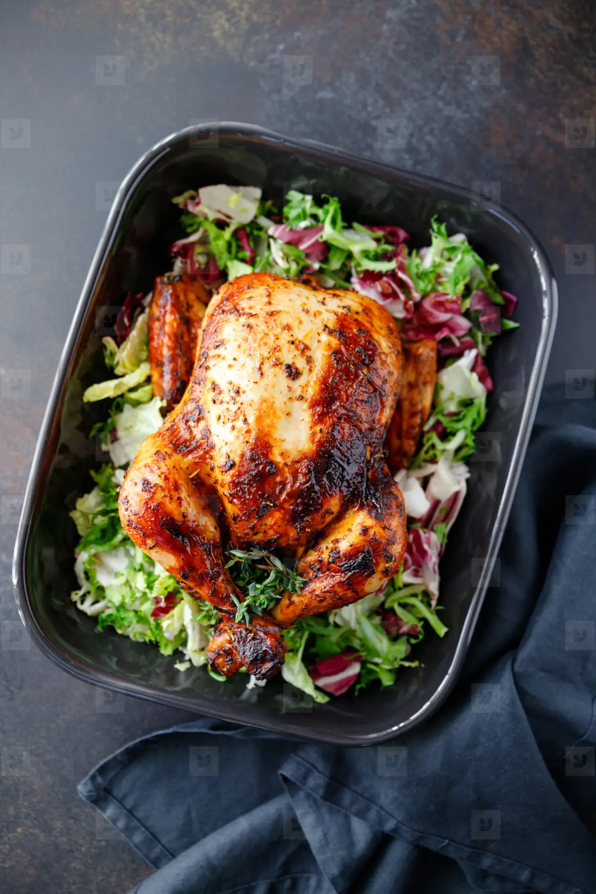 Top view of whole roasted chicken with fresh salad in black dish