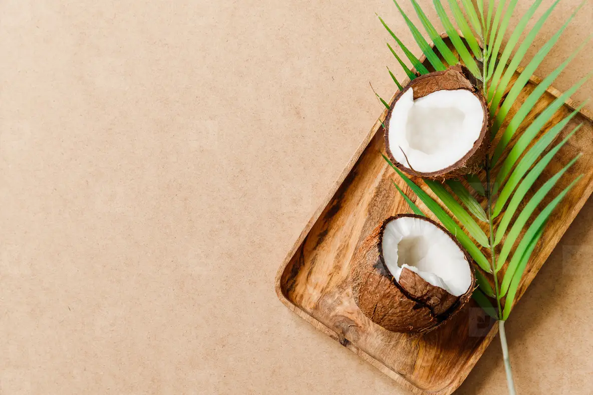 Summer abstract creative composition with coconut a on wooden tray and palm leaf over kraft paper
