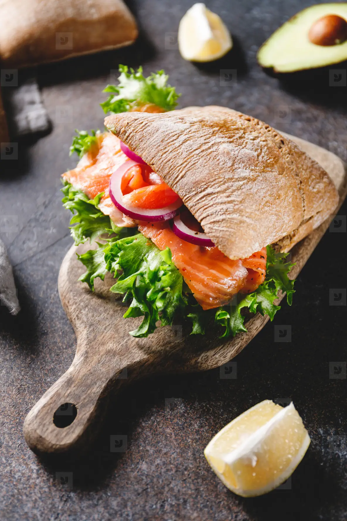 Healthy sandwich with rye bread bun  salmon  avocado  onion and salad served on a wooden rustic board
