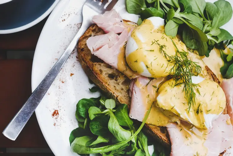 Breakfast with poached eggs on bread with ham, square crop