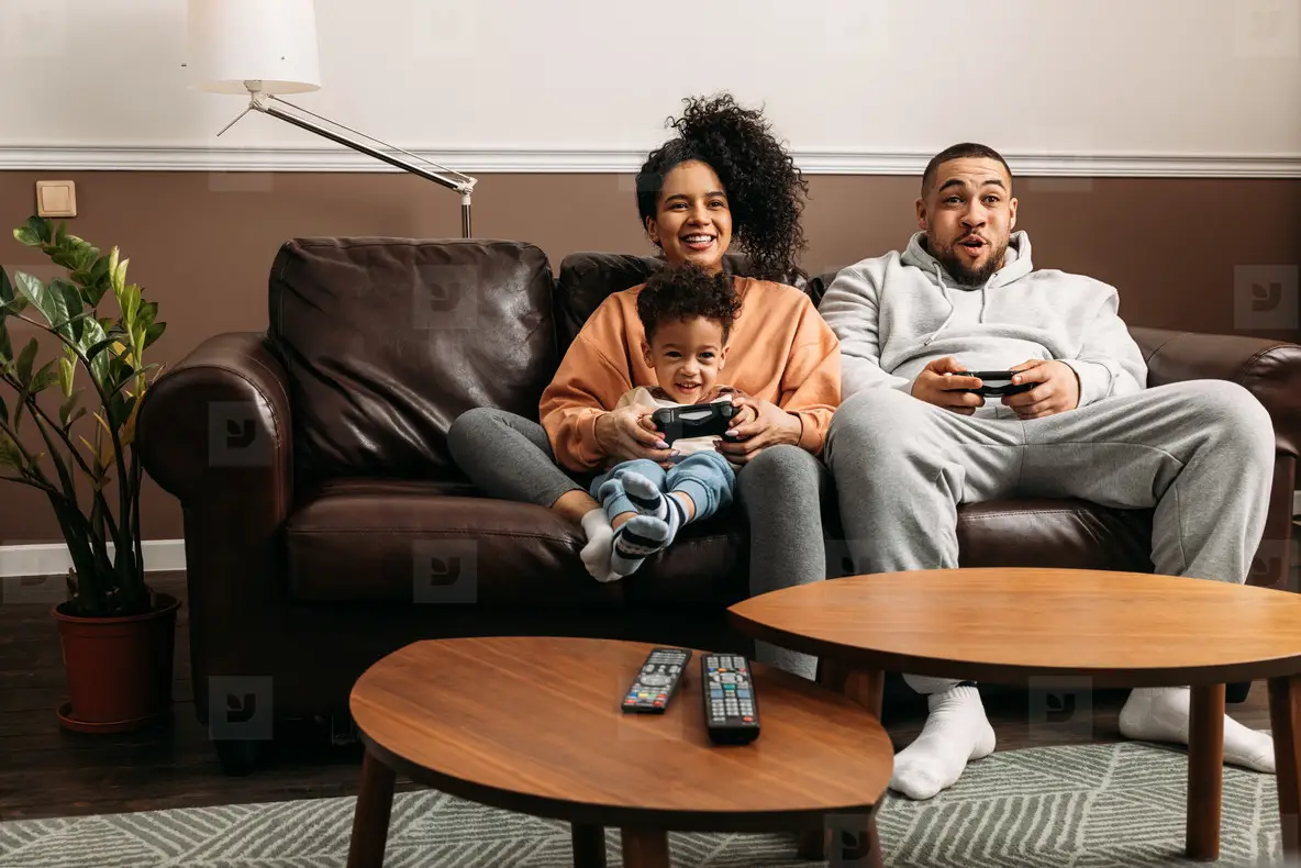 Happy parents with son playing video game  Family of three spending time together on couch at home