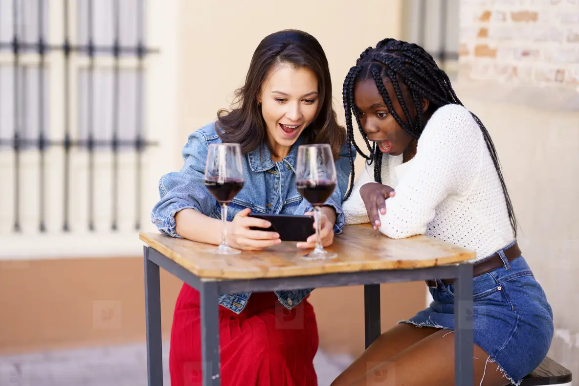 Two Women Looking At Their Smartphone Together While Having A Glass Of Wine  Photo (229065) - YouWorkForThem, image size:1184x789