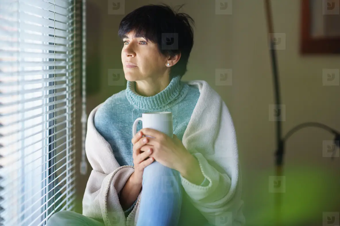 Mid adult woman drinking coffee and looking out of the window in winter day