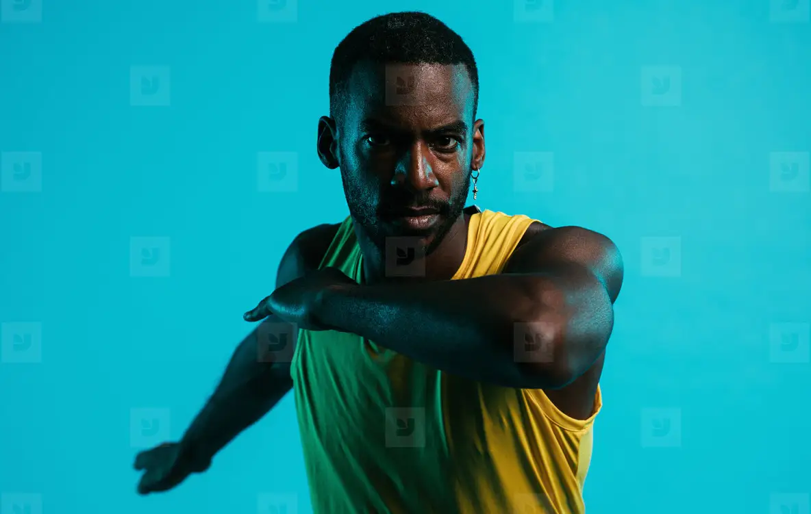 Close up of serious and sweated athlete doing stretching exercises in the studio over blue background
