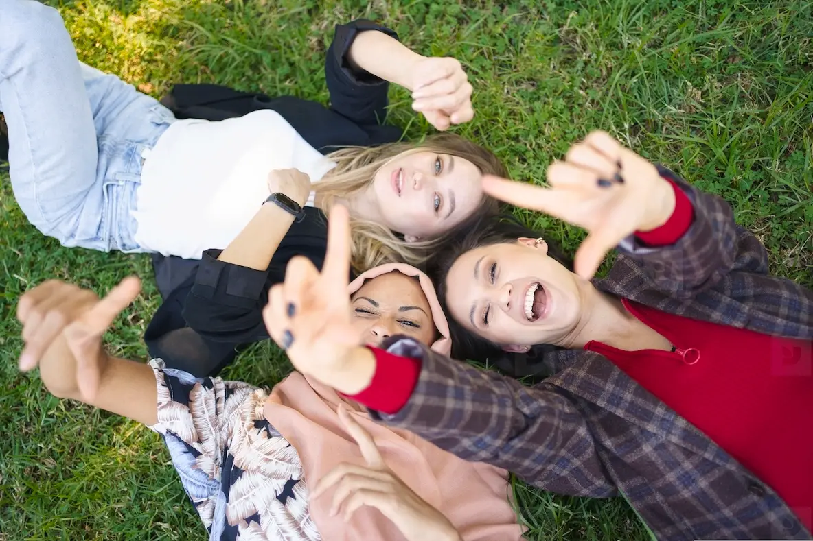 Cheerful ladies gesturing camera while lying on grass