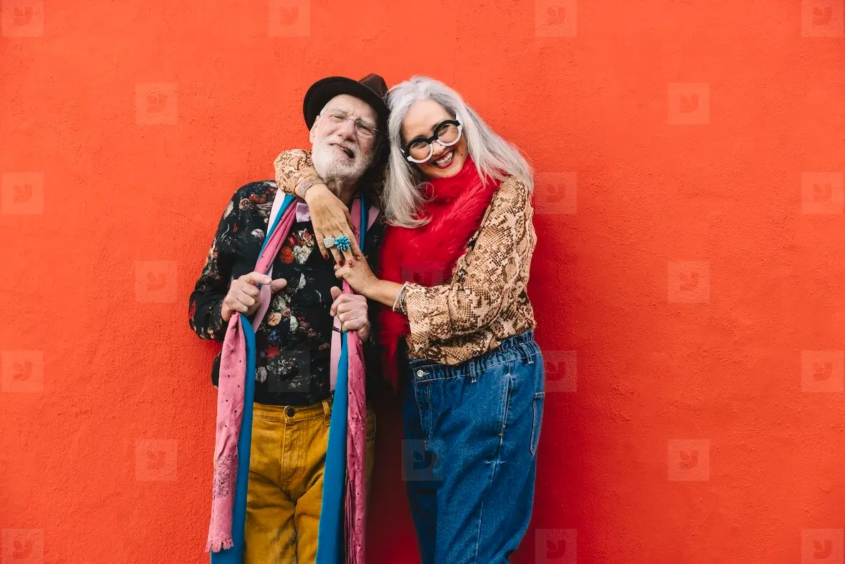 Happy elderly couple smiling cheerfully against a red wall