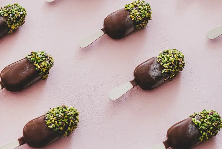 Chocolate glazed ice-cream pops with pistachio icing, square crop
