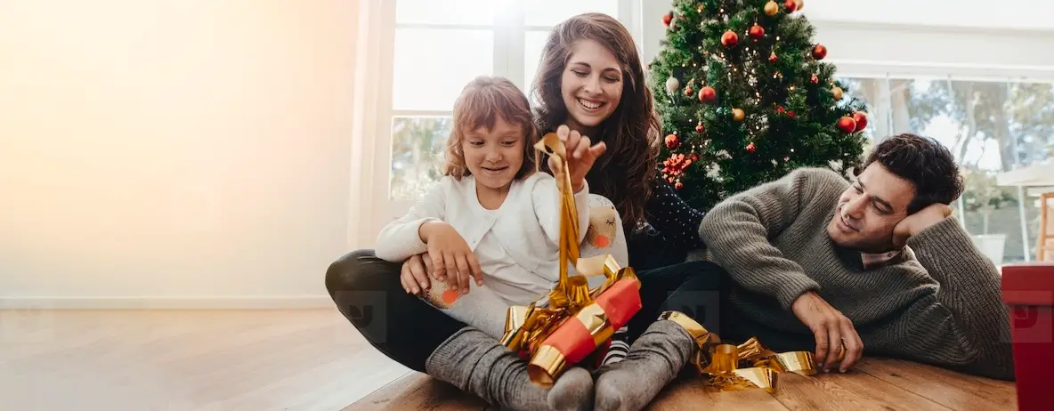 Family Opening Gifts By The Christmas Tree On Christmas Morning