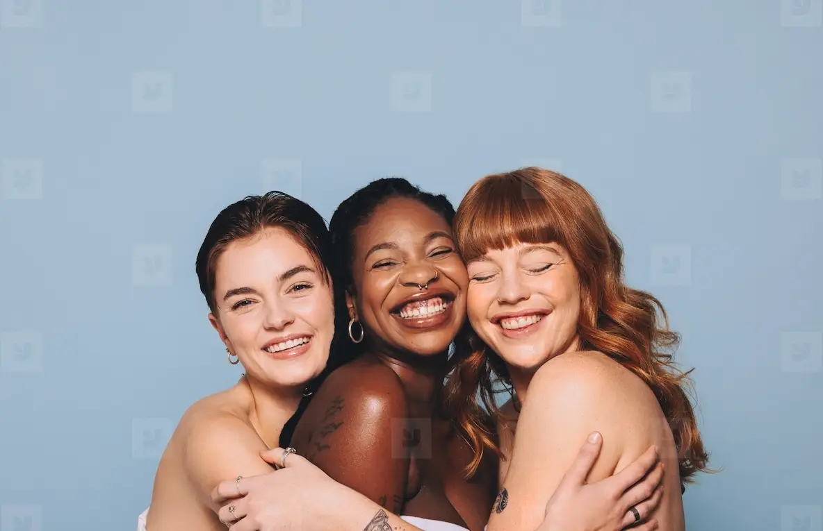 Group of happy women with different skin tones smiling and embracing each other in a studio