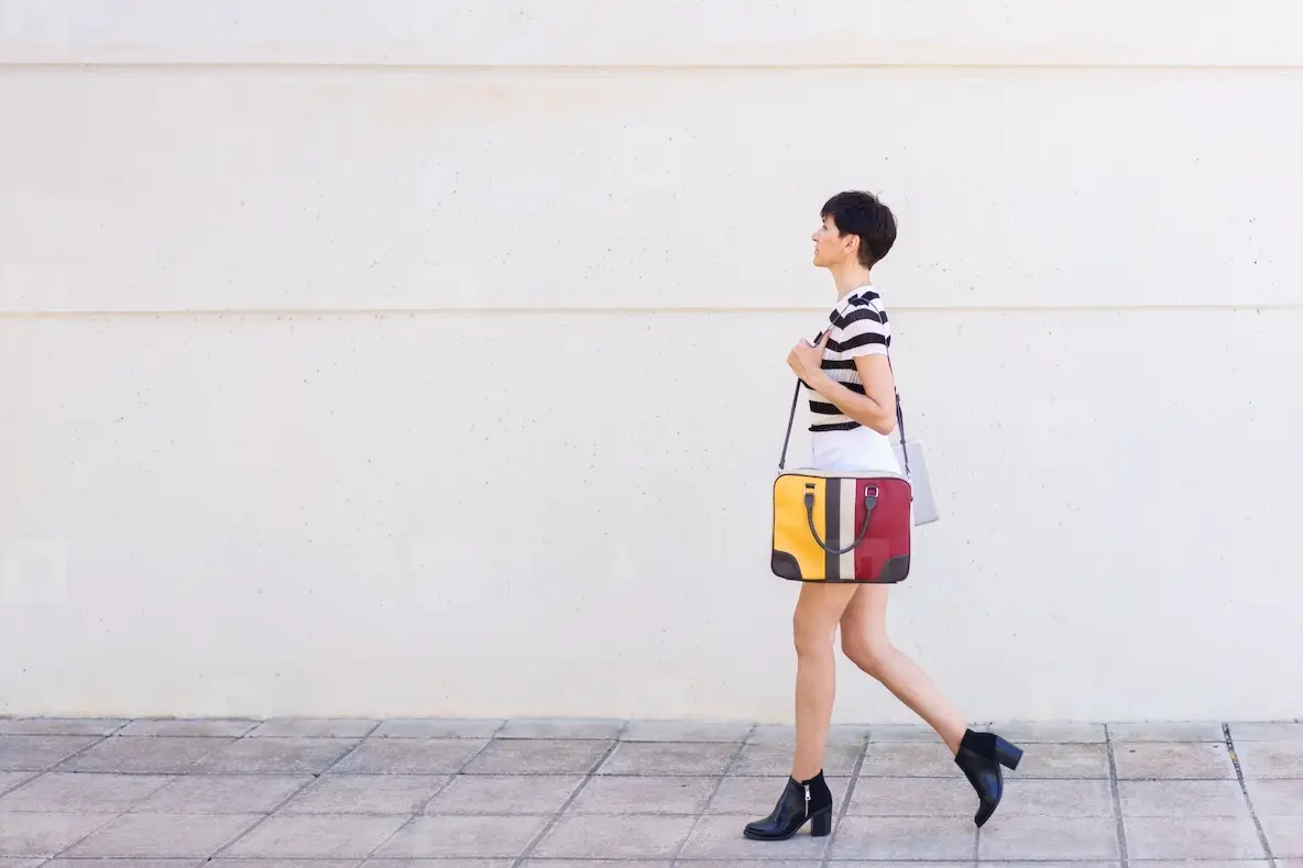 Stylish woman walking on pavement with bag