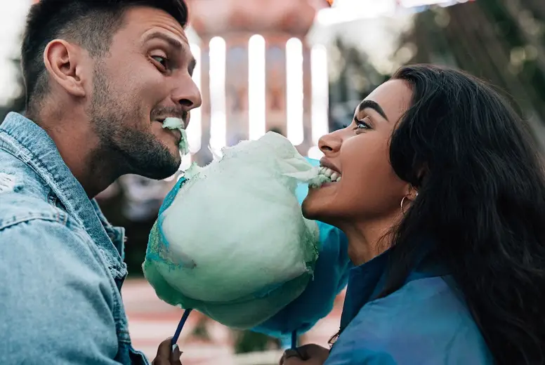 Side view of a boyfriend and girlfriend having fun and biting cotton candy