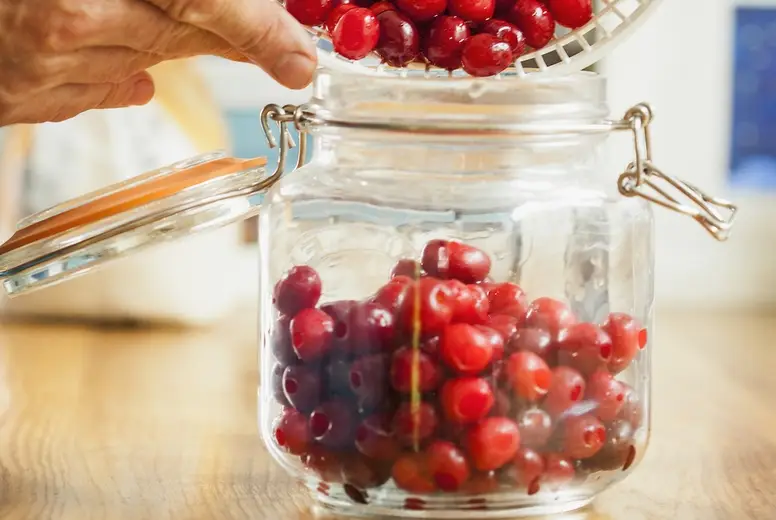 Man Pouring Cherries in a Mason Jar Close-up view
