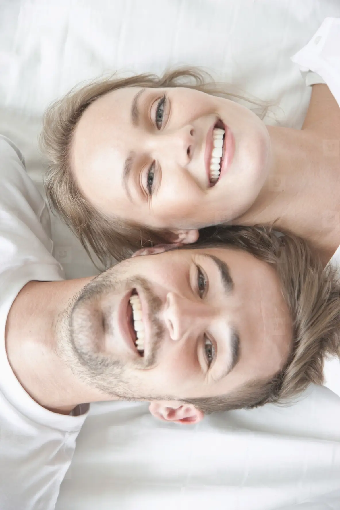 Smiling Couple Lying on Bed Facing Opposite Directions