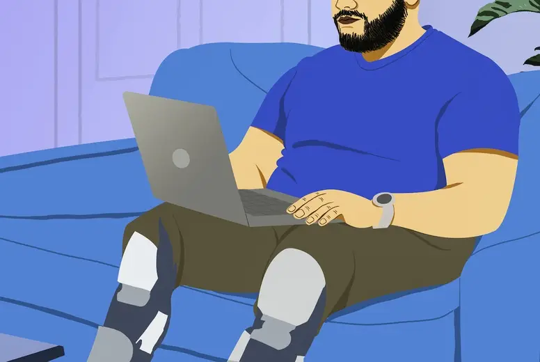 Man with prosthetic legs working from home at laptop on living room sofa