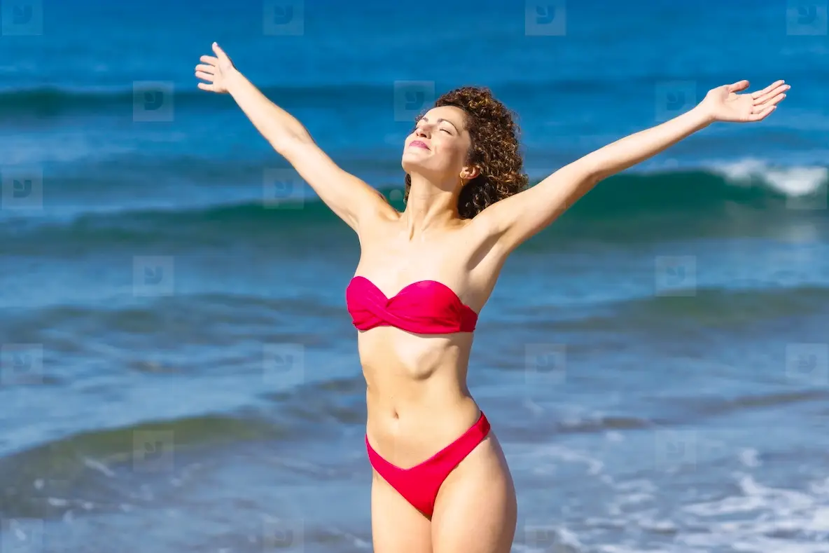 Happy slim woman in bikini with raised arms