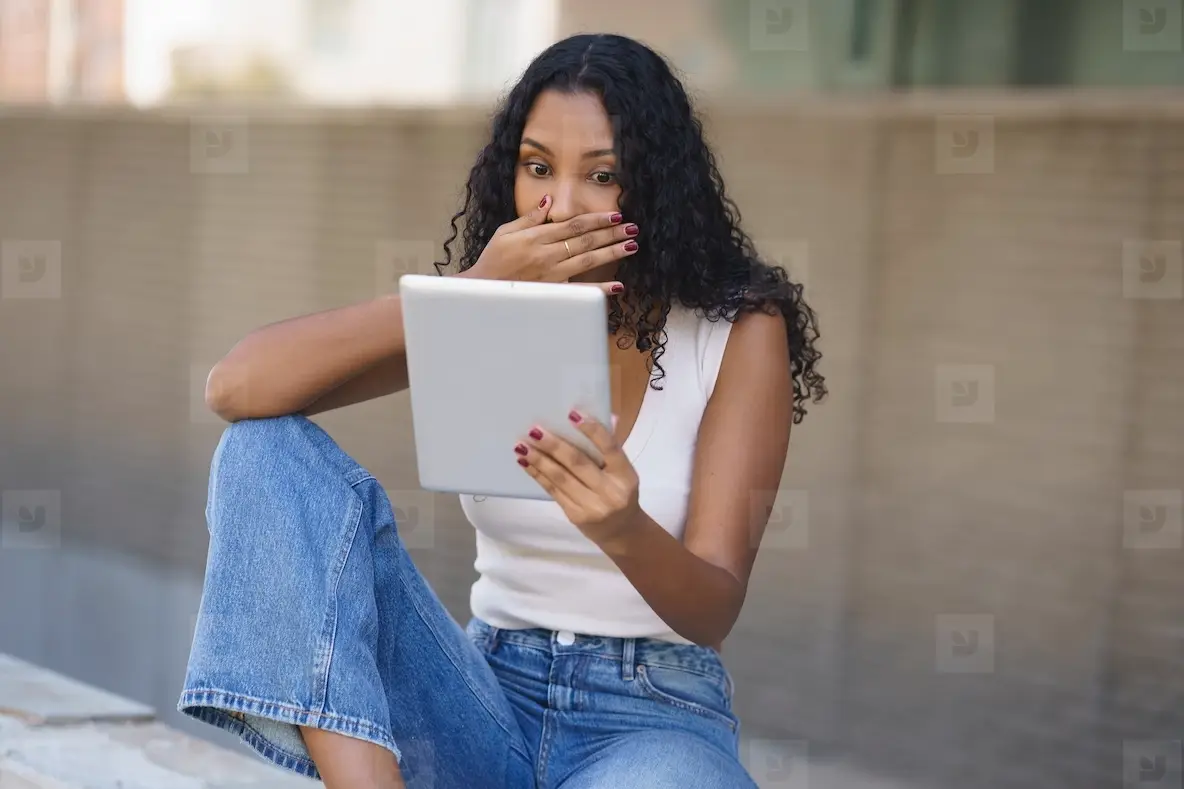A Surprised Young Woman Engaging with a Tablet While Sitting in a Beautiful Outdoor Setting