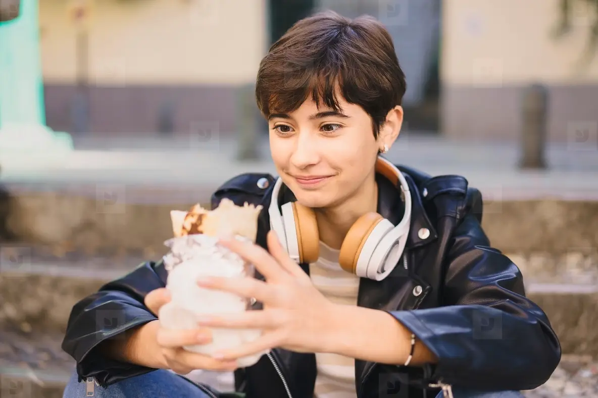 A Young Woman Fully Enjoying a Delicious Dessert While Wearing Headphones in an Urban Setting