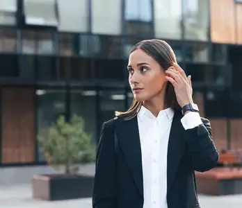 Young female in formal wear looking away and adjusting her hair while standing outdoors