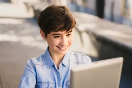 A Young Woman Happily Utilizing Her Laptop Outdoors While Enjoying the Beautiful Day