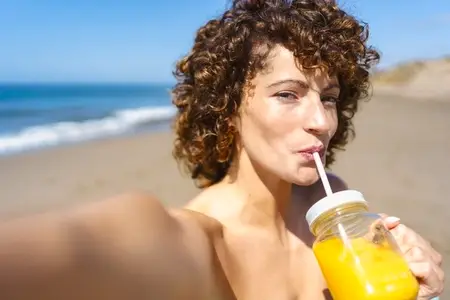 Young woman drinking fresh juice on beach