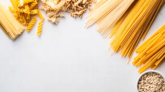Various dried pasta types neatly arranged on white surface