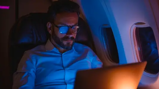 Man working on laptop during flight  focused and illuminated by screen light