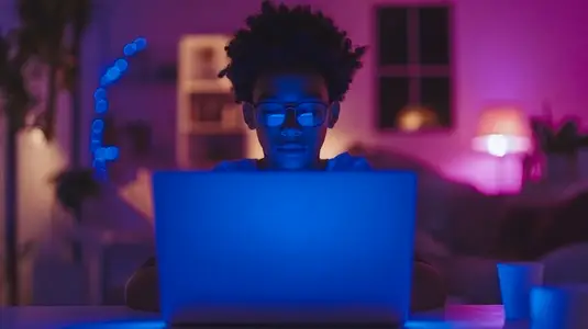 Teenager focused on laptop in dimly lit room with blue light