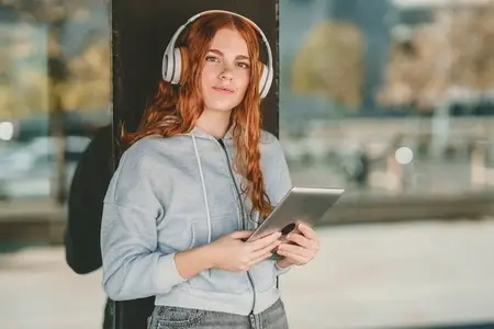 A Young Woman Wearing Headphones Enjoying Music While Using a Tablet Device to Relax