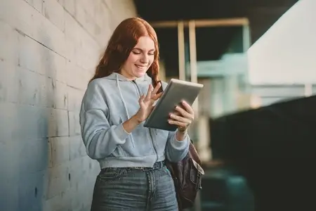 A young woman is happily engaged with her tablet while in a vibrant urban setting