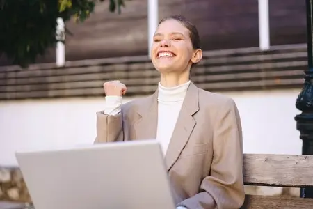 A Joyful Businesswoman is Happily Celebrating Her Success Outdoors Near a Bench in Nature